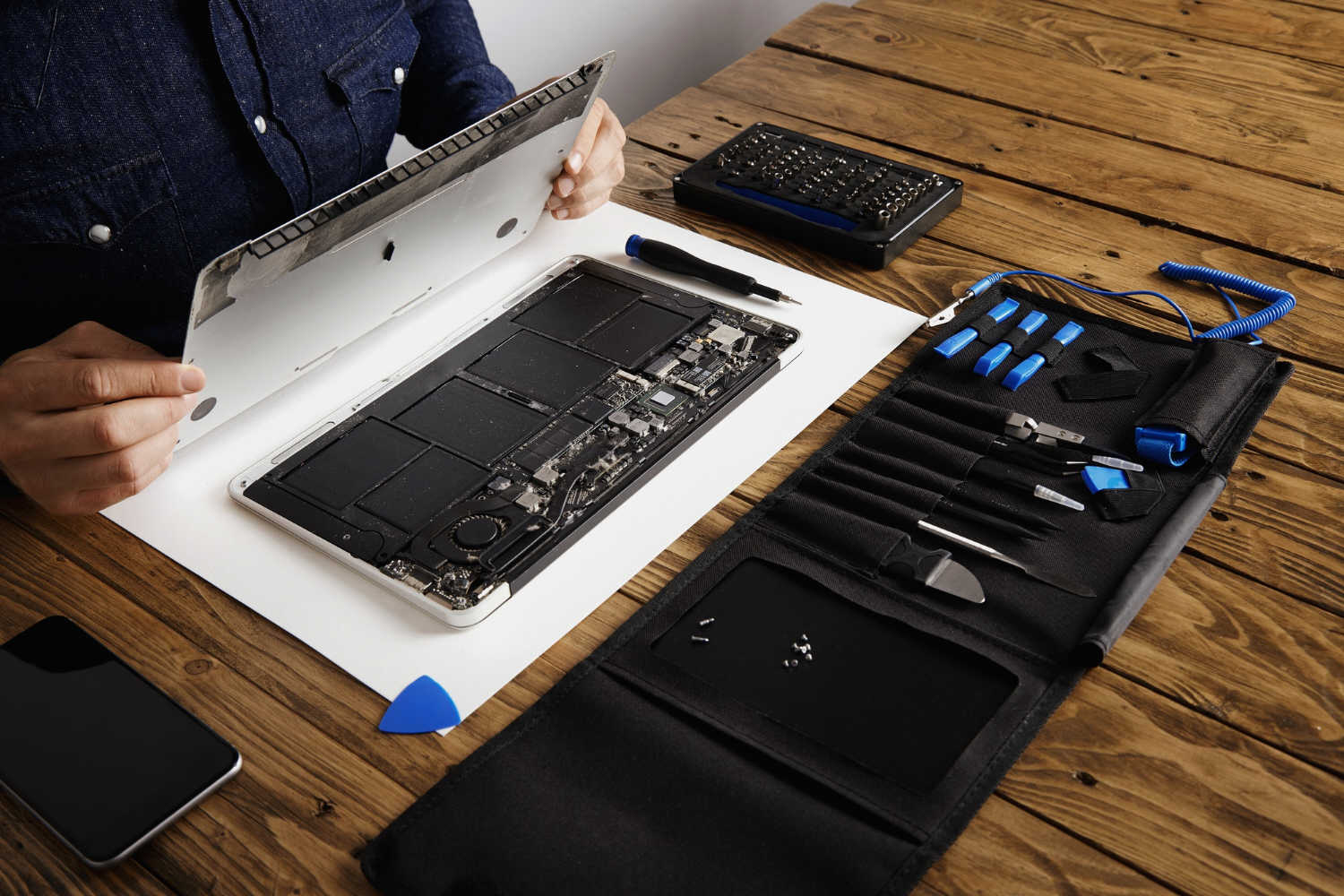 serwisant otwiera tylna pokrywe gornej czesci laptopa przed naprawa czyszczeniem i naprawa za pomoca swoich profesjonalnych narzedzi z pudelka z narzedziami w poblizu drewnianego stolu